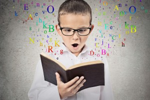Surprised child reading a book with letters flying away from it isolated on grey wall background. Face expression. Education concept