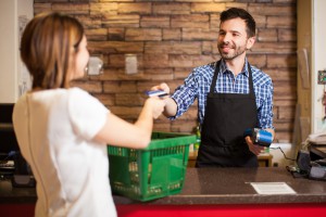 Handsome young man with a beard taking a credit card from a customer at a grocery store