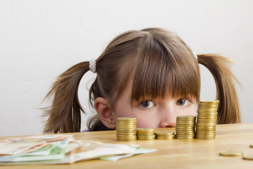 Mädchen schaut auf Geldtürme - auf dem Tisch liegend
