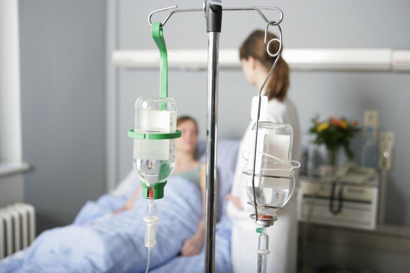 Close-up of IV drip with patient and doctor in background
